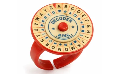 A red plastic vintage decoder ring with a rotating cream-colored dial showing letters A through Z paired with blue cipher symbols around a small red center knob.