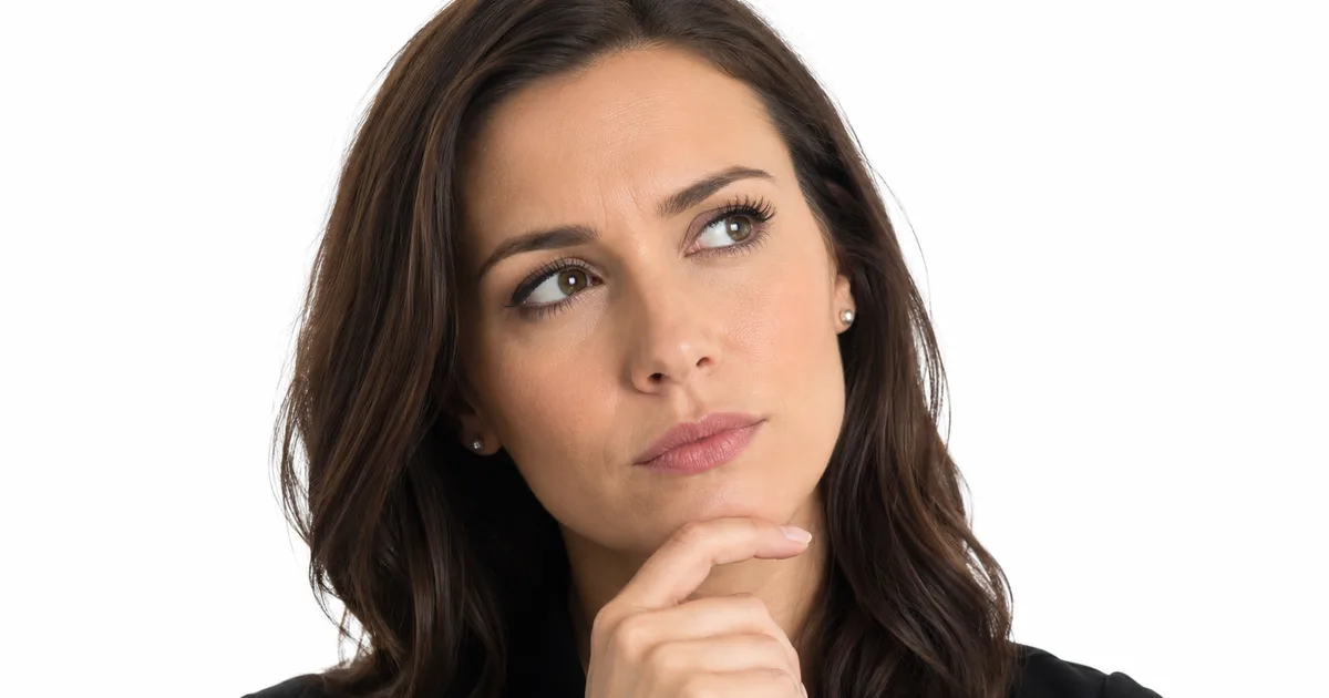 A woman in a black blazer rests her hand on her chin and glances upward with a skeptical, thoughtful expression against a white background.