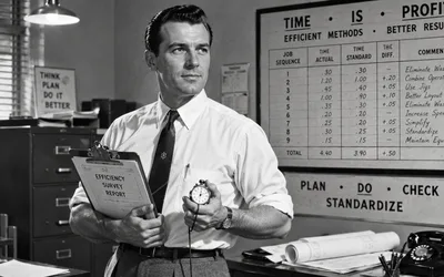 A man in a white dress shirt and dark tie stands in a mid-century office holding a clipboard labeled Efficiency Survey Report and a stopwatch, with a time-study chart and Plan Do Check Standardize sign behind him.