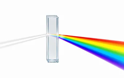 A clear glass prism on a white background, with a single thin beam of white light entering from the left and separating into a broad rainbow spectrum that fans out to the right.